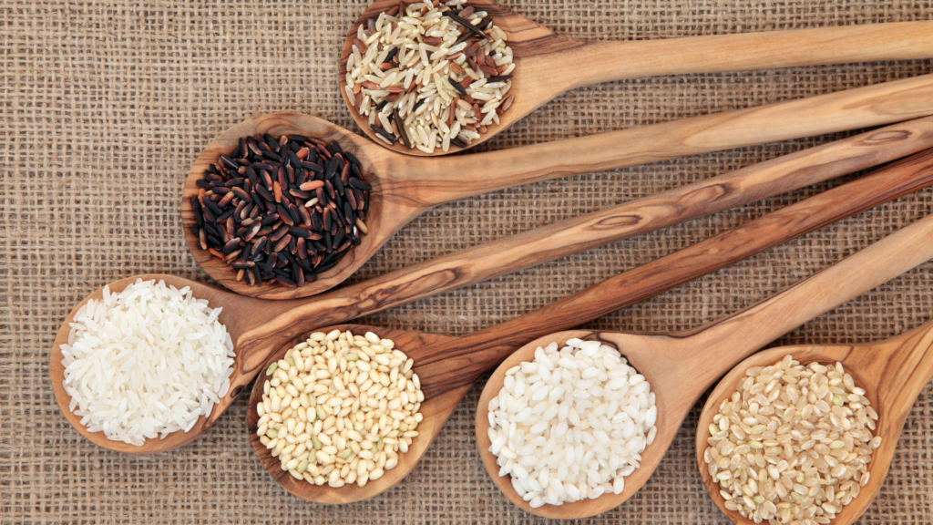 Culinary diversity in rice: A variety of rice grains (black, brown, white, basmati, and Arborio) displayed in wooden spoons on a burlap background. Discover the global and cultural impact of rice in our culinary journey article