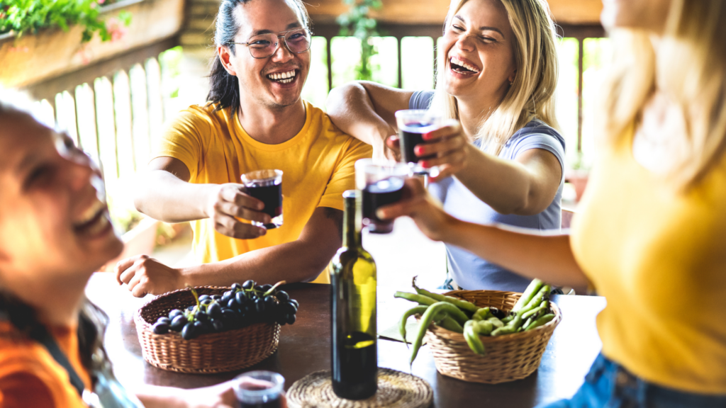 A group of friends enjoying a wine tasting experience at an outdoor setting during a culinary land tour. The joyful scene features fresh produce on the table and several people raising their glasses in a toast.