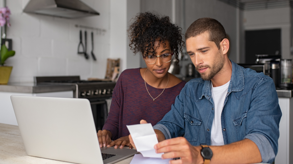 couple looking thoughtfully at a laptop and a  note trying to determine if they should travel