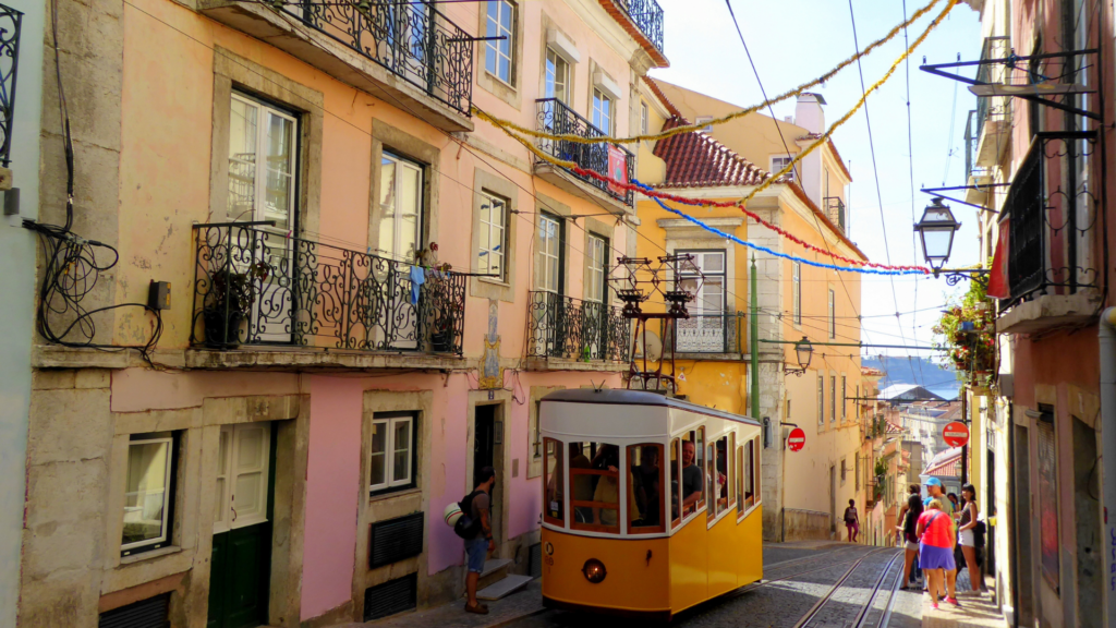 us Yellow Trams going uphill in Lisbon riding by beautiful historic architecture in Portugal where you will be immersed in culture and cuisine.