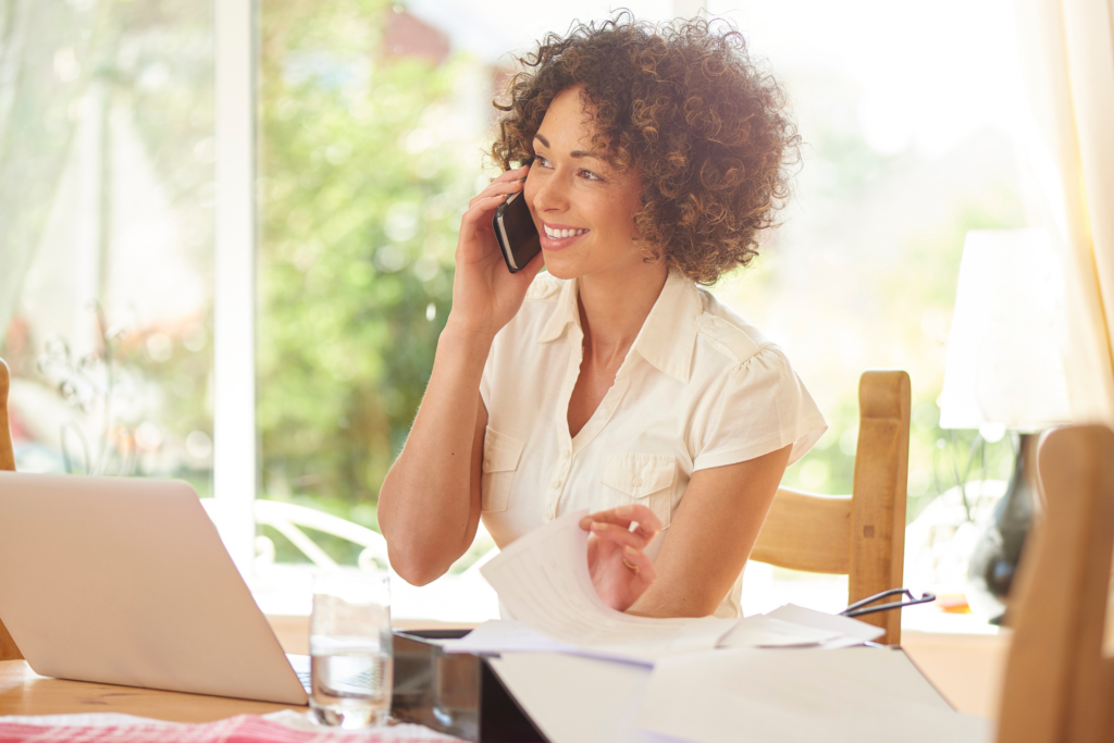 Lady smiling on the phone while facing her laptop while researching Travel Insurance