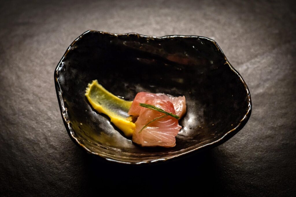 Exquisite raw fish crudo artfully plated in a black bowl, showcasing gourmet cuisine for luxury foodie travel.